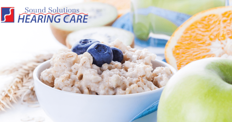 A bowl of oatmeal, a green apple, an orange, and other healthy foods.