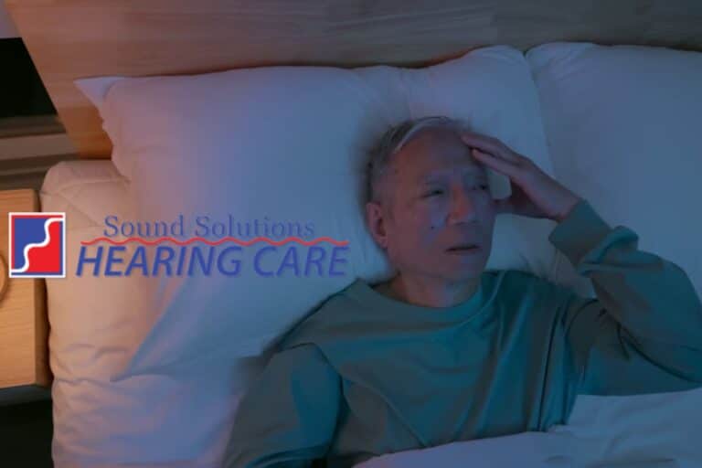 man laying in bed holding his head in pain